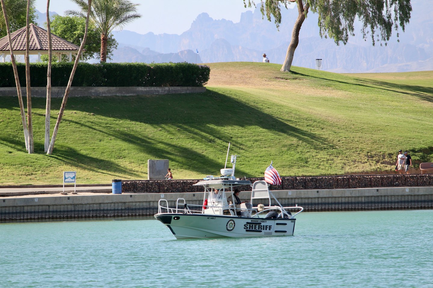 A sheriff patrol boat navigates water near a grassy hillside.