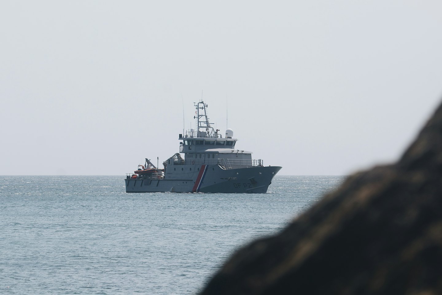 Grey patrol boat with red, white, and blue stripe on calm ocean.
