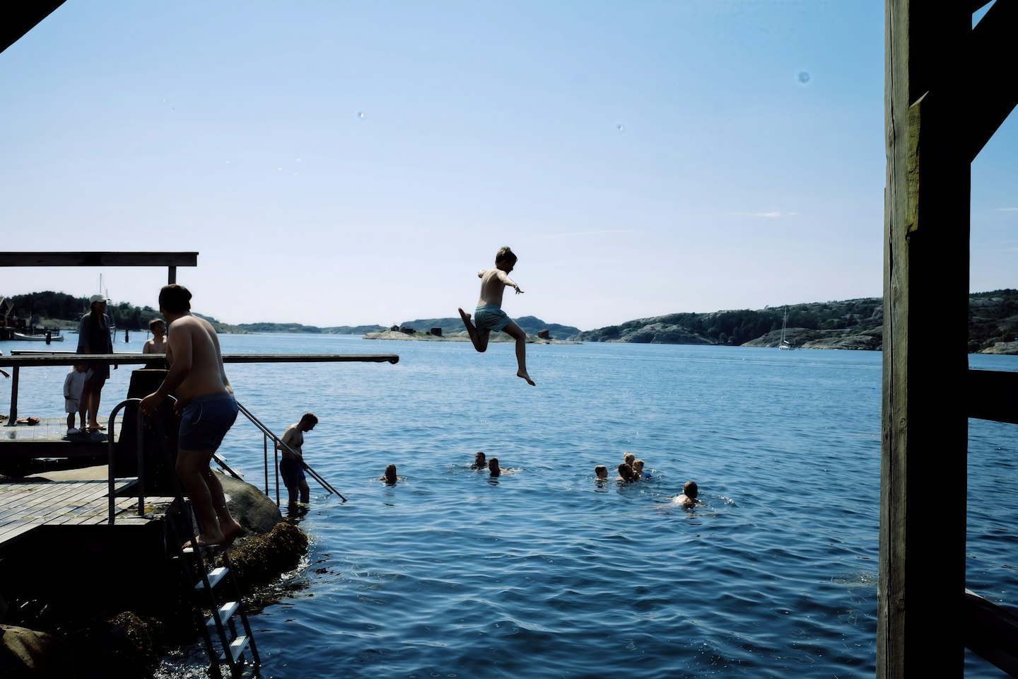 People swim and jump from a wooden dock into the sea.