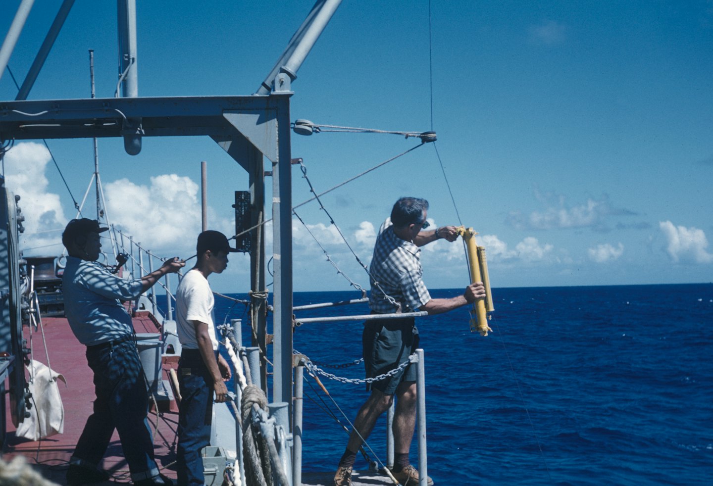Three researchers conduct scientific work on a vessel deck.